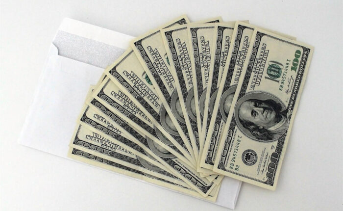 Mehrere 100-Dollar-Scheine fächerförmig auf einem weißen Umschlag ausgelegt.
