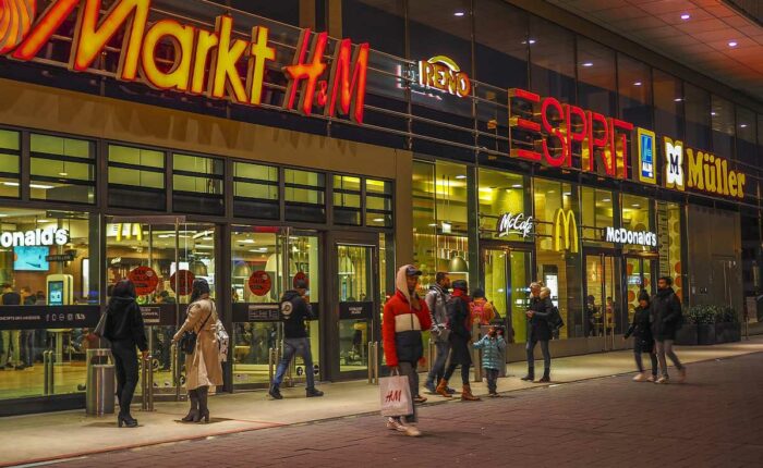 Menschen vor einer beleuchteten Einkaufspassage am Abend.