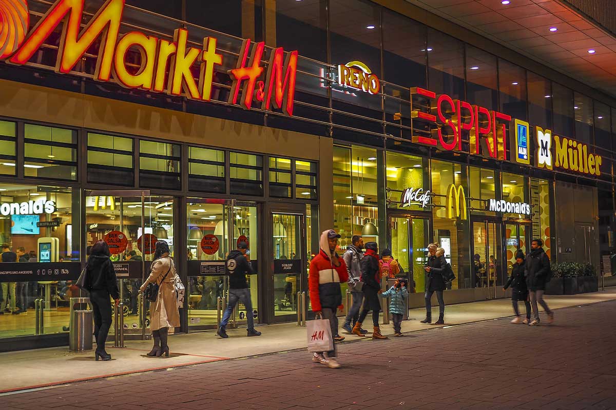 Menschen vor einer beleuchteten Einkaufspassage am Abend.