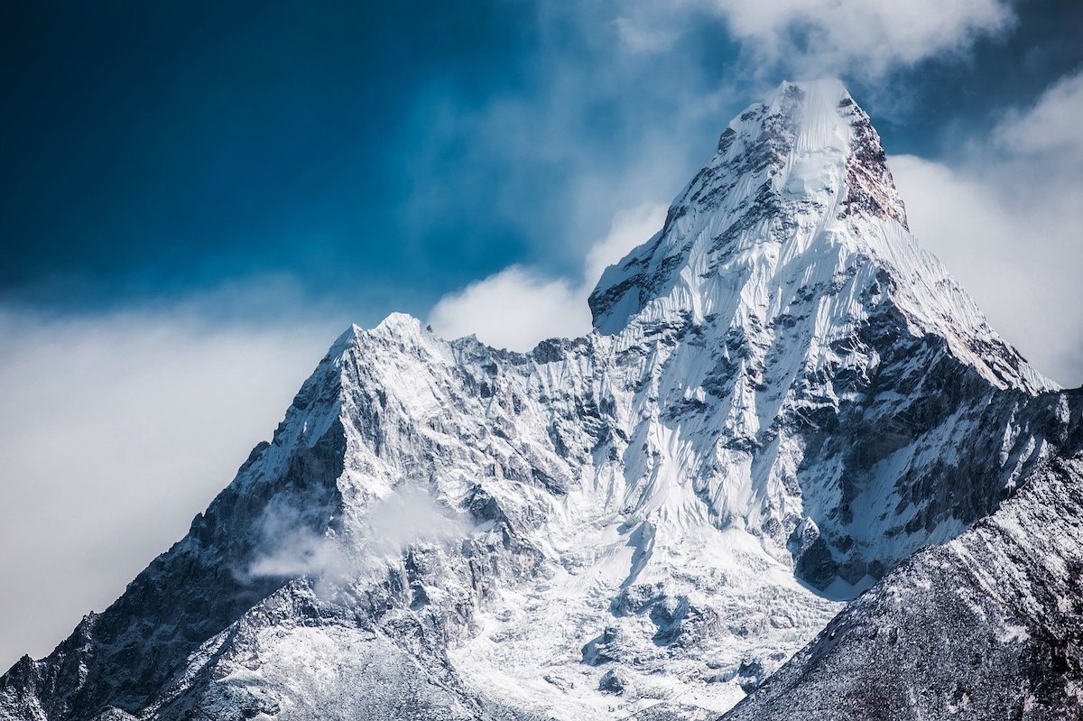 Schneebedeckter Berggipfel mit leichter Wolkenbildung an den Hängen.
