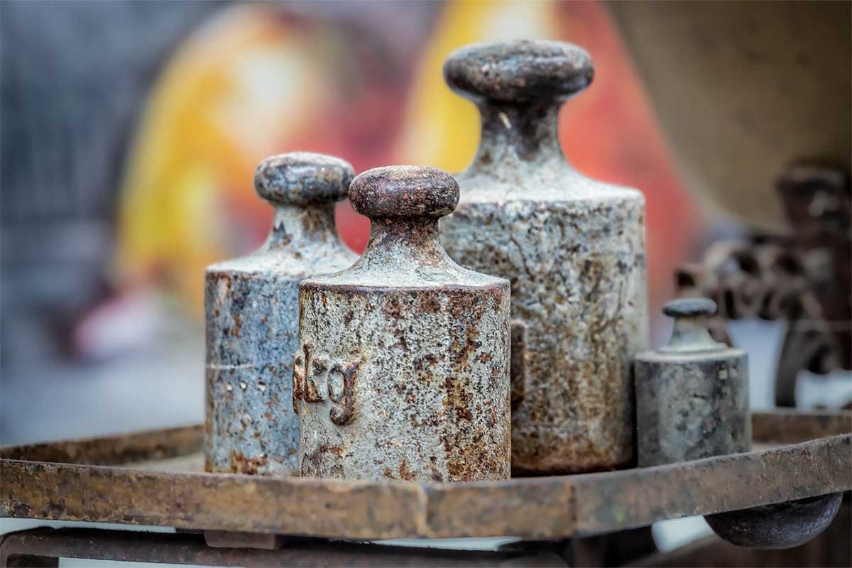 Mehrere alte, rostige Metallgewichte auf einer mechanischen Waage.