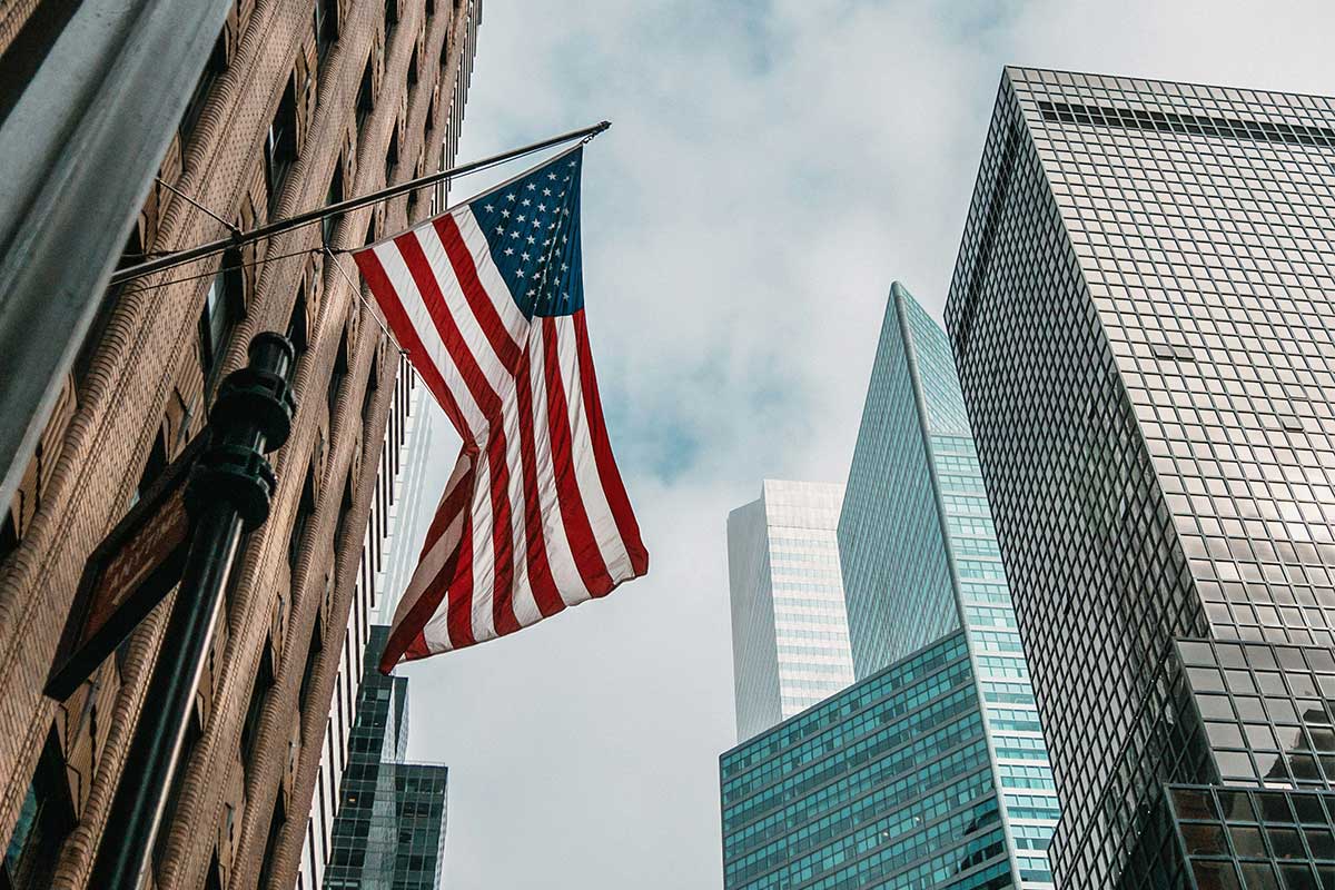 US-Flagge vor modernen Hochhäusern in einer amerikanischen Innenstadt.