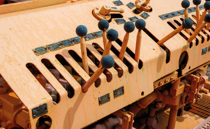 Nahaufnahme vieler Steuerhebel mit blauen Griffen auf einem rostfarbenen Industriesteuerpult.