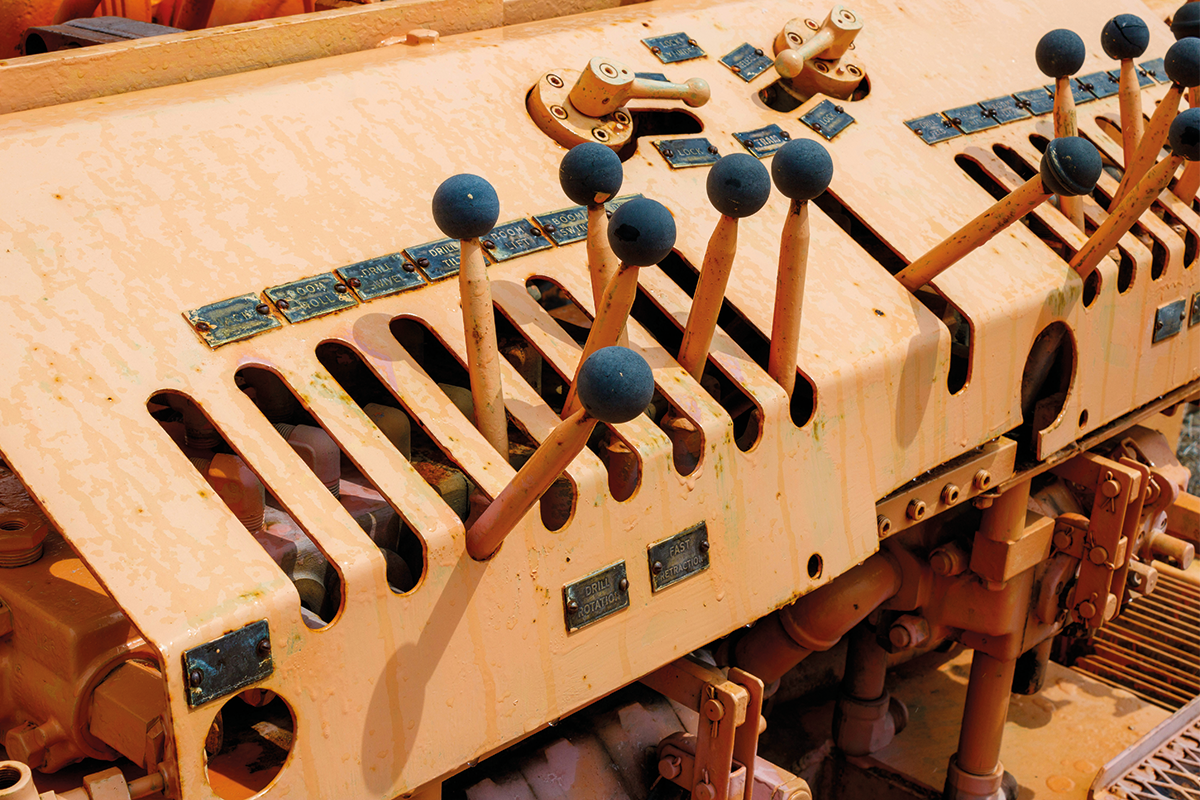 Nahaufnahme vieler Steuerhebel mit blauen Griffen auf einem rostfarbenen Industriesteuerpult.