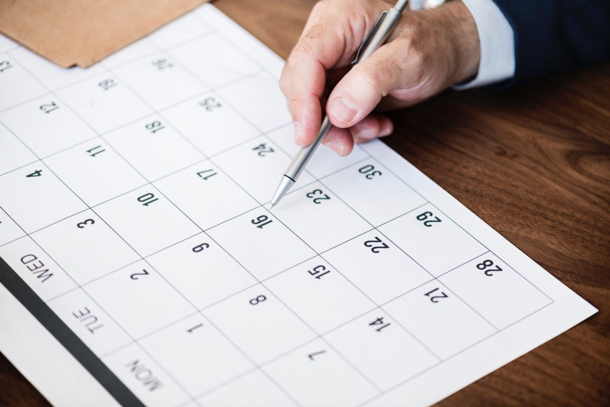 Männliche Hand markiert mit einem Stift Termine auf einem Papierkalender.