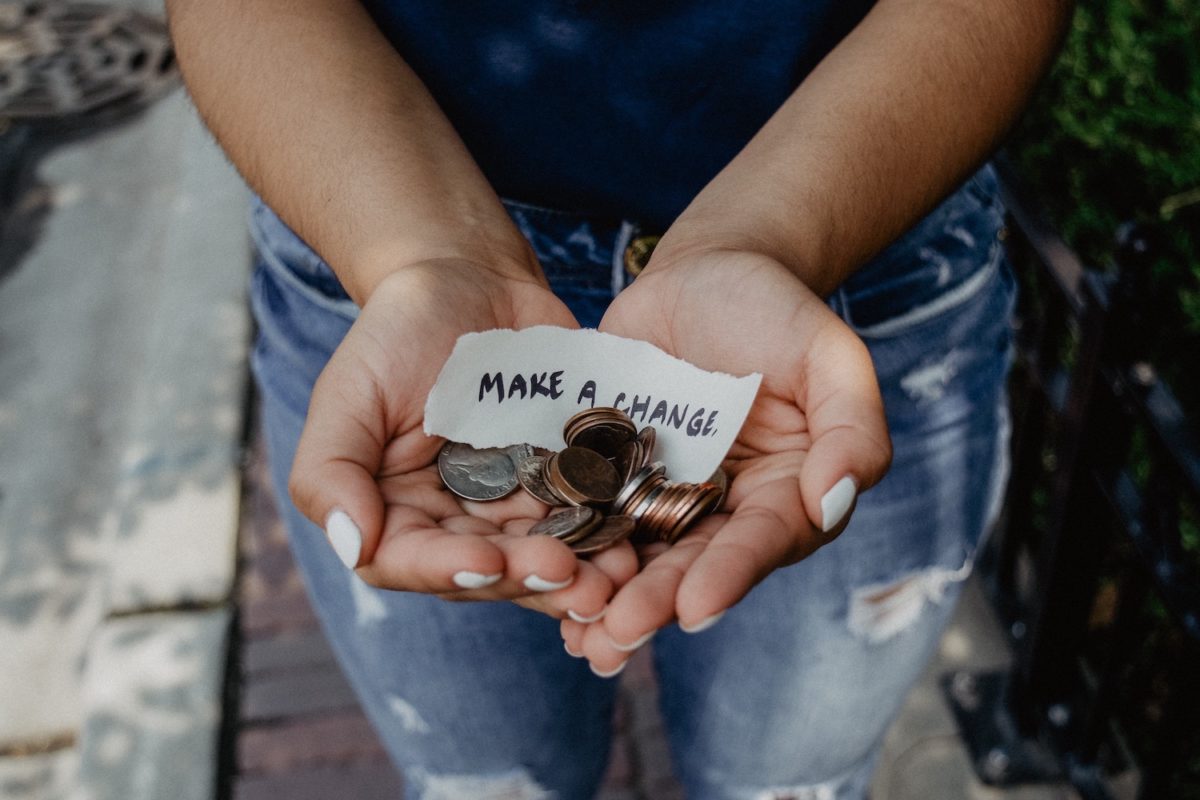 Person hält Kleingeld und ein Papier mit Aufschrift "Make a change" in der Hand.